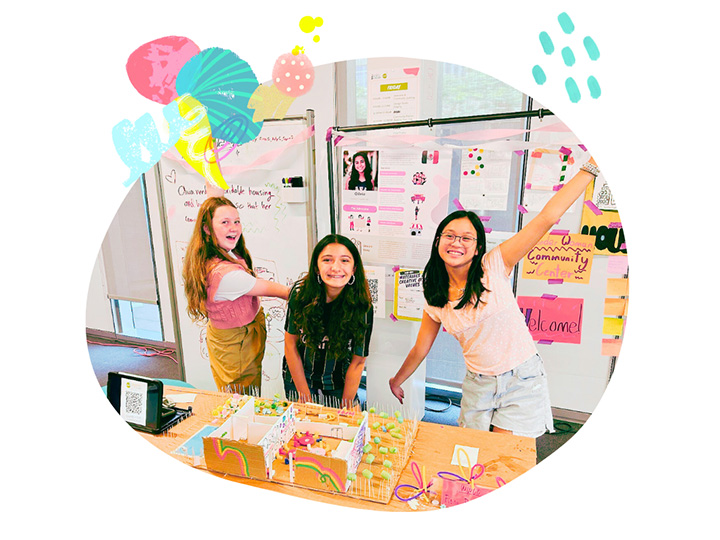 Three SEED students proudly showing off their final project, Wonder Woman Community Center.